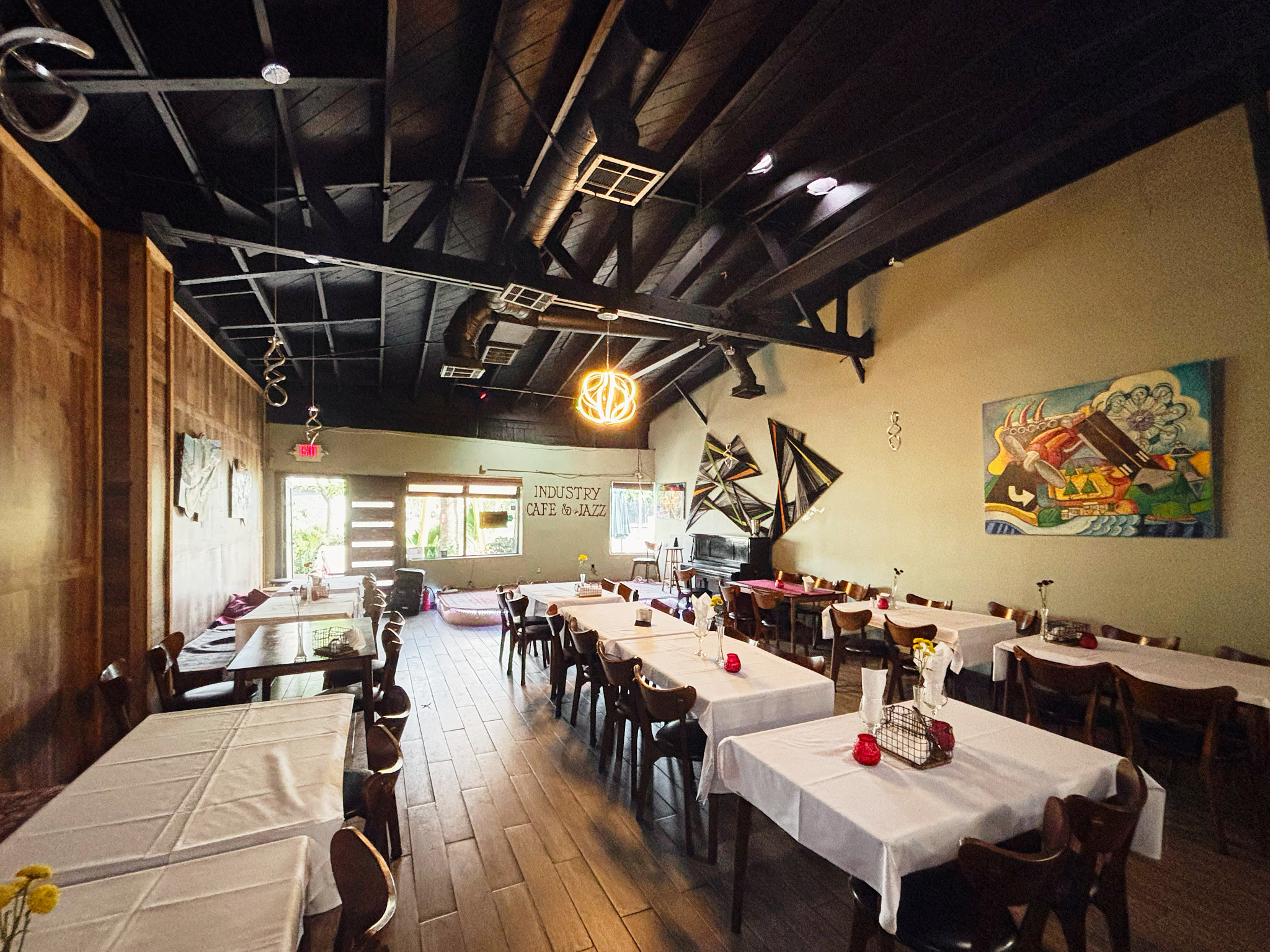 Interior of Industry Cafe and Jazz showing dining tables with white tablecloths, wooden chairs, artwork on the walls, and a stage area at the back