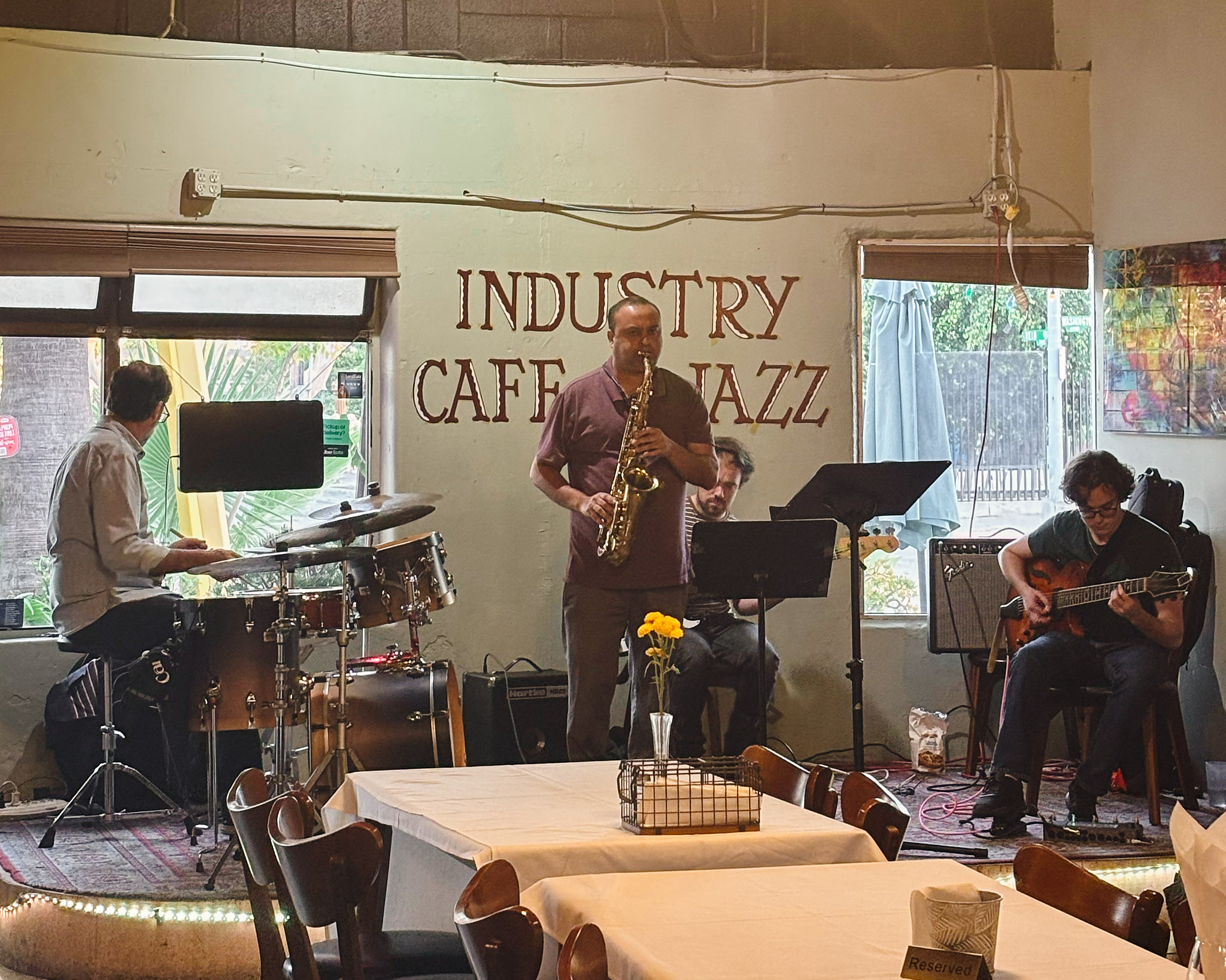 Live jazz band performing on stage at Industry Cafe and Jazz, with musicians playing saxophone, drums, keyboard, and guitar in front of seated tables