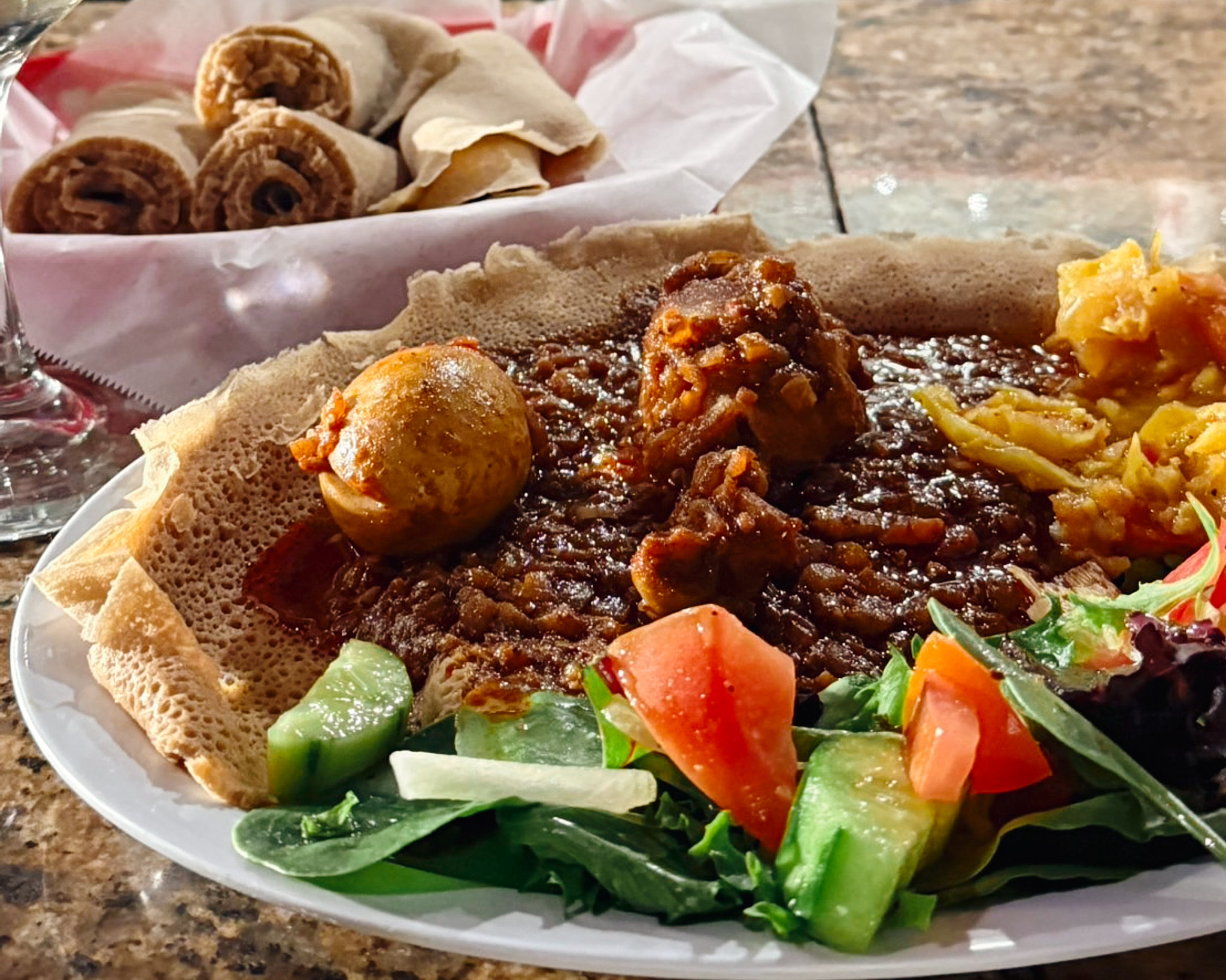 Plate of Ethiopian-style food with stew, boiled egg, vegetables, salad, and rolled injera bread served on a large platter