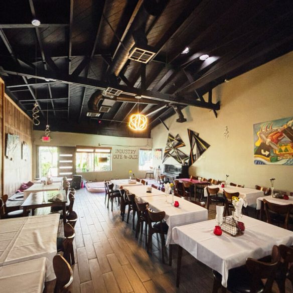 Interior of Industry Cafe and Jazz showing dining tables with white tablecloths, wooden chairs, artwork on the walls, and a stage area at the back